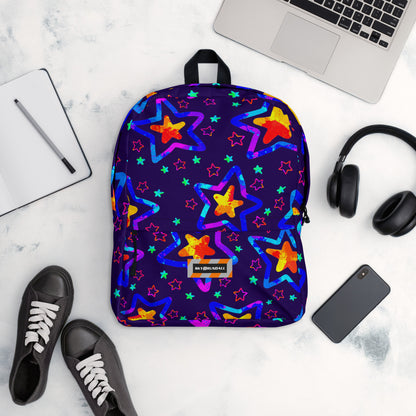 Backpack with colorful star pattern on a marble surface with a laptop, headphones, and shoes.