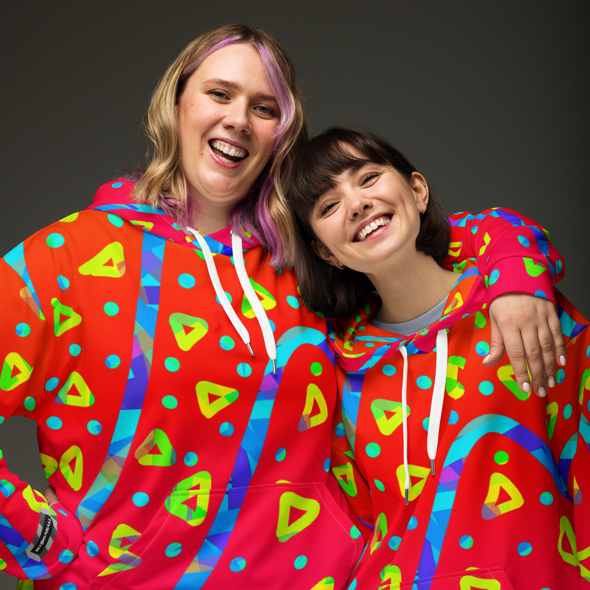 Two people wearing colorful red hoodies with geometric patterns on a dark background