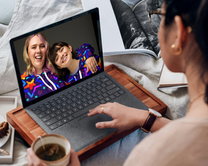 Person using a laptop with two people on a video call displayed on the screen, sitting on a couch.